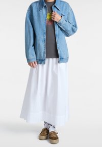 Jasnoniebieska kurtka dżinsowa na szarej koszulce z grafiką, w połączeniu z zwiewną białą spódnicą i brązowymi butami w zwierzęcy wzór. Białe skarpetki z logo.