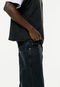 Zwarte denim jeans met een losse pasvorm, gecombineerd met een donkergrijze mouwloze top. De stof lijkt zacht met een matte textuur. Zichtbare zijnaad.