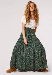 Floral maxi skirt with a green background, featuring yellow and pink patterns, smocked waist, and tiered design. Paired with tan suede boots.