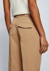 Beige wijde broek met achterste flapzakken, met een gladde textuur en een subtiele glans. Tailleband met het merk "BOSS".
