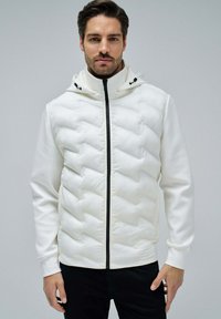 White zipped hoodie with a puffy, quilted texture, featuring a hood and black zipper details. Smooth fabric with a fitted silhouette.