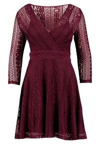 Bordeaux jurk met een V-hals, lange kanten mouwen, gestructureerde stof en gepatineerde accenten. Uitlopende rok met kantdetails aan de zoom.
