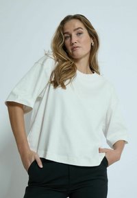 White cropped t-shirt made of cotton, featuring short sleeves and a round neck. The fabric appears smooth and soft, with a relaxed fit.
