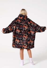 Pārmērīgi liela melna kapuce ar florālu un pūķa rakstu oranžā, sarkanā un bēšā krāsā. Izgatavota no mīksta, pūkaina materiāla ar platiem piedurknēm.