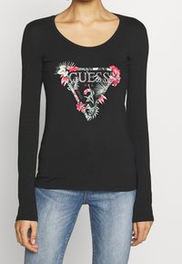 Maglietta nera a maniche lunghe con un logo triangolare decorato con fiori e la scritta "GUESS U.S.A." in argento, realizzata in tessuto morbido e con un design aderente.