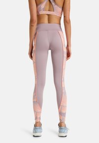 Legginsy o jasnofioletowej bazie z różowymi wzorami liści oraz kontrastującymi pomarańczowymi szwami bocznymi, wykonane z elastycznego materiału sportowego.