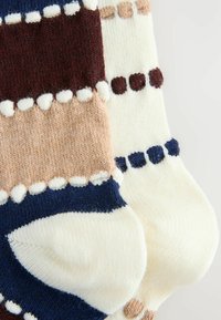 Pletené ponožky s viacfarebnými pruhmi v námorníckej modrej, burgundskej, krémovej a svetlohnedej farbe, so strapcami pozdĺž hornej hrany. Mäkká textúra.