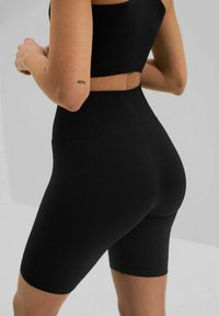 Černá žebrovaná sportovní souprava zahrnuje krátký top a šortky s vysokým pasem. Materiál má texturu s hladkým povrchem a elastickým pasem.