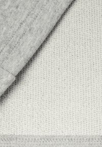 Šedý okraj látky překrývá texturovaný bílý povrch. Šedá má hladký povrch, zatímco bílá má pletený, texturovaný vzhled.