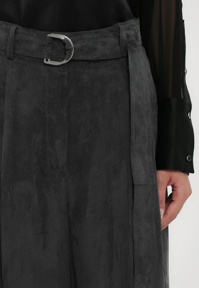 Pantaloni in suede grigio con una vestibilità a gamba larga, dotati di una cintura con fibbia argentata e tasche laterali. Texture liscia con un delicato effetto lucido.
