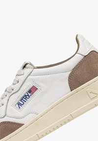 Sneaker bianco in pelle con accenti in suede marrone, linguetta testurizzata e una patch con logo che presenta rosso e blu. Suola in gomma crema con design del battistrada.