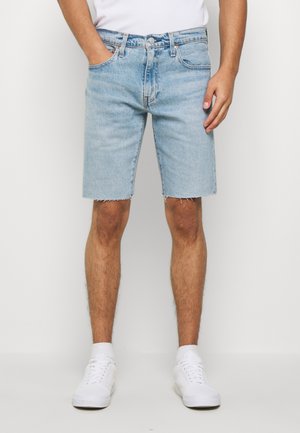 Shorts en denim bleu clair avec un ourlet effiloché, design à cinq poches et coupe slim, associés à des baskets blanches et un t-shirt blanc ajusté.