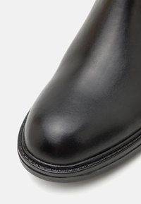Bota de cuero negro con punta redondeada, textura suave y un sutil detalle de costura a lo largo de la suela para mayor refuerzo.