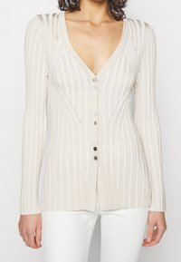 Beige geribde cardigan met een V-hals, knoopsluiting en lange mouwen. Bevat een textuurstof en subtiele diagonale stikdetails.