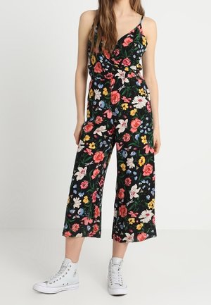 Kwiatowy kombinezon na czarnym tle, ozdobiony czerwonymi, różowymi i żółtymi kwiatami. Skrócone szerokie nogawki i cienkie ramiączka, zestawione z białymi trampkami.