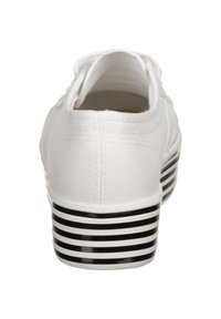 White canvas shoe with a low profile, featuring a black and white striped sole, rounded toe, and visible stitching details.