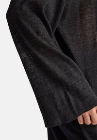 Schwarzer, gestrickter Pullover mit lockerer Passform, weiten Ärmeln und einer Knopfdetaillierung nahe dem Bündchen; weicher Stoff mit leicht durchscheinendem Aussehen.