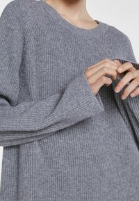 Maglione grigio a coste con scollo rotondo e maniche lunghe e larghe. Presenta una superficie testurizzata e un design dalla vestibilità rilassata.