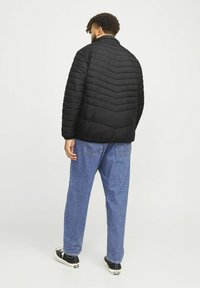 Schwarze gesteppte Jacke mit Zickzackmuster, hohem Kragen und elastischen Bündchen, kombiniert mit hellblauen, weit geschnittenen Jeans und schwarzen Sneakers.