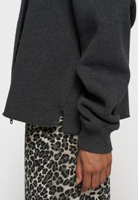 Grijze sweatshirt met een ontspannen pasvorm, geribbelde manchetten en een ruwe randafwerking, gecombineerd met een rok met luipaardprint in gedempte tonen.