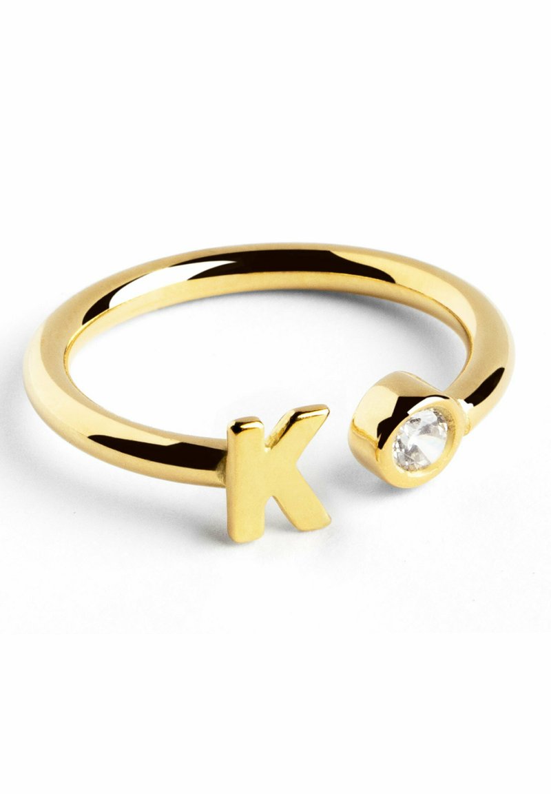 Anillo de oro con una banda redonda, que presenta una 'K' en relieve y un acento de gema clara. Textura suave y acabado pulido.