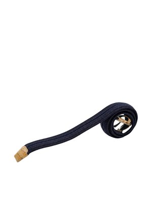 Cintura in tessuto blu navy intrecciato arrotolata a un'estremità con fibbia in metallo argento e punta in pelle color cuoio su sfondo bianco.