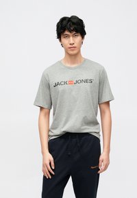 Grå bomull T-skjorte med svart "JACK & JONES"-logo og oransje aksent. Kombinert med mørkeblå joggebukser med subtil brodering.
