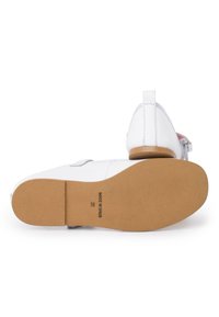 Weiße Lederschuhe mit einer braunen Gummisohle. Sie verfügen über einen Riemen und minimale Nähte, mit einem rosa und grauen Akzent an der Rückseite.