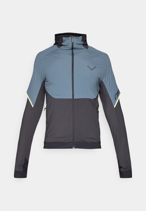 Veste zippée grise et noire avec un col haut, coupe athlétique, panneaux supérieurs texturés et accents réfléchissants sur les manches.