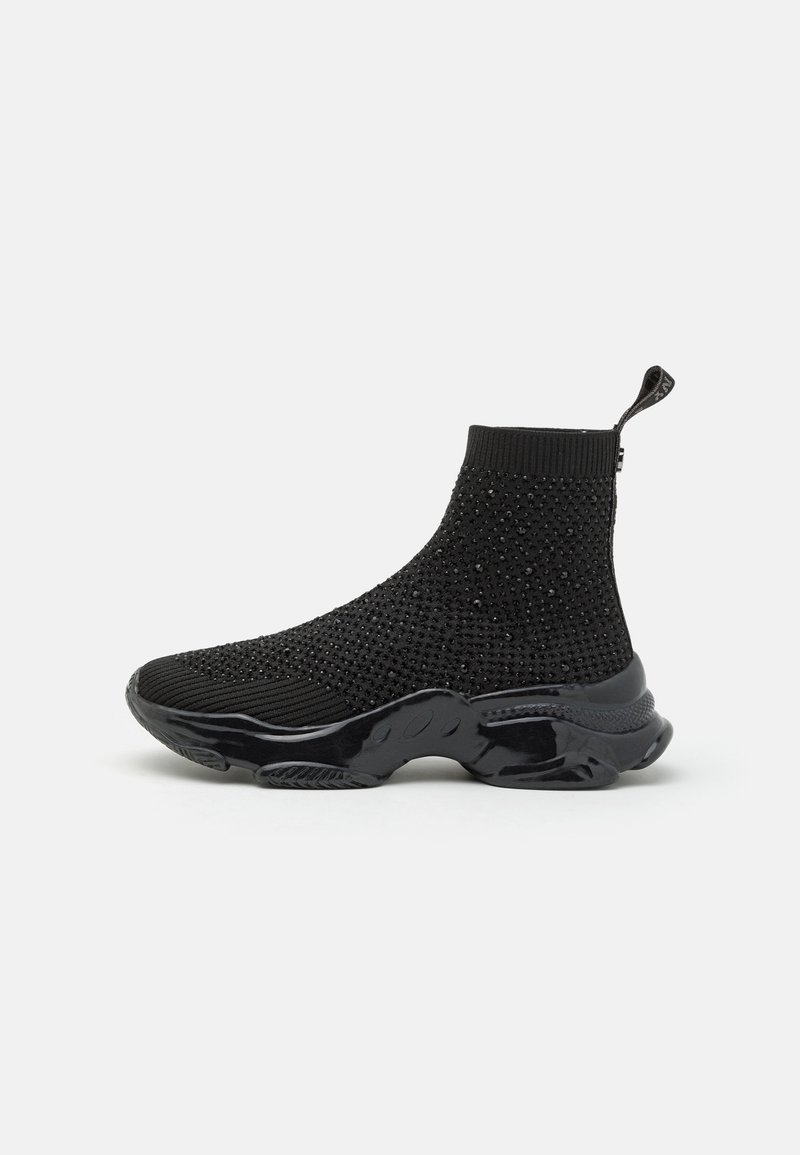 Baskets type chaussettes montantes noires avec tige en maille texturée, embellissements cloutés, languette au talon et semelle épaisse brillante.
