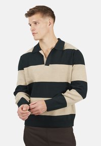 Sweter w paski z poziomymi ciemnozielonymi i beżowymi paskami, z kołnierzykiem z patką oraz ściągaczami przy mankietach i dole.