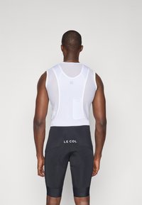 Weißes ärmelloses Jersey mit Netzstruktur, kombiniert mit schwarzen Radshorts mit einem Logo. Einfaches und funktionales Design für sportliche Zwecke.