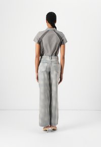Camisa gris de manga corta con paneles laterales en contraste, combinada con unos jeans de pierna ancha descoloridos. Tejido suave con ligero desgaste en los jeans.