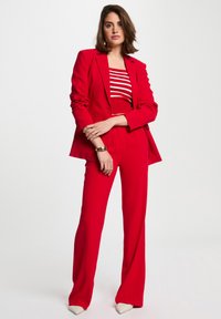 Rood pak met een op maat gemaakt blazer en flared broeken. De top heeft horizontale witte strepen. De schoenen zijn puntig en crèmewit.