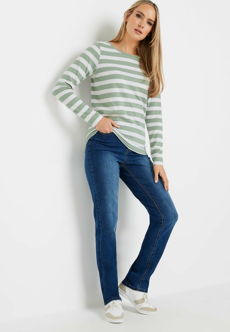 Grün-weißer gestreifter Langarmshirt, kombiniert mit blauen Jeans und weißen Sneakers. Das Shirt hat einen runden Halsausschnitt und seitliche Schlitze.