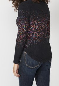 Černý pletený svetr s živým vícebarevným vzorem, který přechází od ramenní části k lemu. Obsahuje kulatý výstřih a bo ční rozparky.