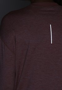 Bordeauxfarbener Hoodie aus strukturiertem Material mit einem weißen vertikalen Streifen-Detail auf der Rückseite in der Nähe des Kragens.