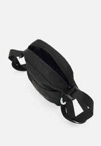 Borsa a tracolla in tessuto nero con zip superiore, cinturini regolabili e un sottile dettaglio del logo. Texture liscia, design compatto.