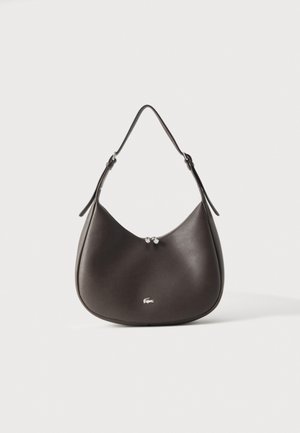 Sac à bandoulière en cuir marron foncé, avec une partie supérieure arrondie, une fine bandoulière, un fermoir argenté et un petit logo crocodile, sur fond uni.