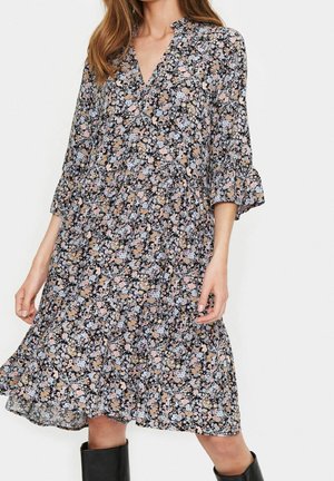 Blumenkleid mit schwarzem Hintergrund, das mit rosafarbenen, blauen und beigen Blumen verziert ist. V-Ausschnitt, dreiviertel Ärmel und ein ausgestellter Saum.