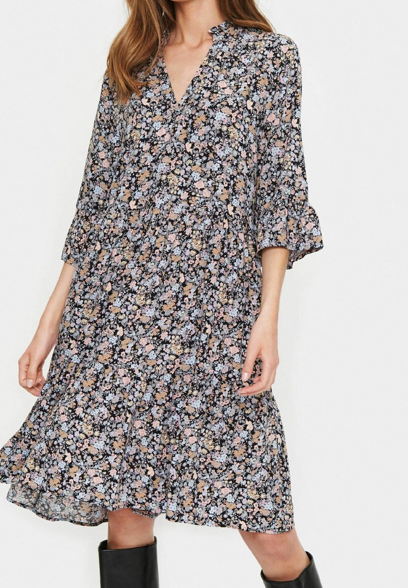 Blommig klänning med svart bakgrund, prydd med rosa, blå och beige blommor. V-hals, tre kvart ärmar och utsvängd fåll.