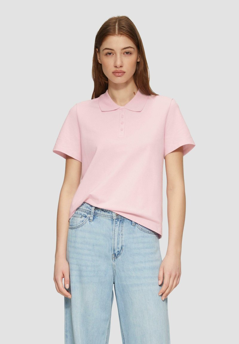 Lichtroze polo met korte mouwen en kraag, voorzien van een knopenlijst met drie knopen, gecombineerd met lichtblauwe, loszittende spijkerbroeken.