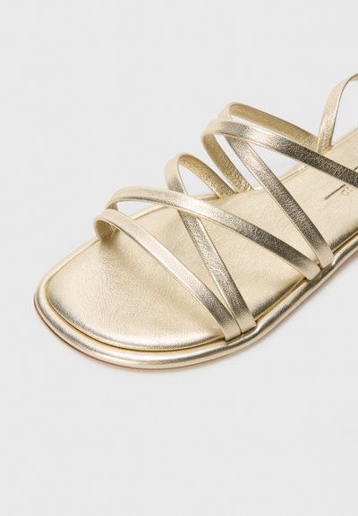 Gullmetalliske flate sandaler med flere kryssende stropper, en jevn tekstur, og design med firkantet tå og en minimalistisk såle.