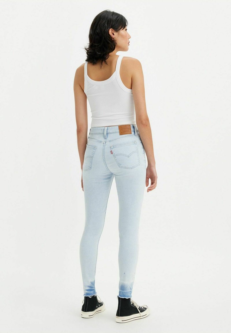 Helle blaue Skinny-Jeans mit hoher Taille, ausgestattet mit einem Lederpatch auf der Rückseite, fransigen Knöchelsäumen und einer glatten Textur.