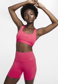 Fuksia spordikomplekt, mis koosneb istuvast spordirinnakorvist ja kõrge vöökohaga lühikestest pükstest. Valmistatud siledast ja venivast materjalist, millel on hõbedased Nike logo.