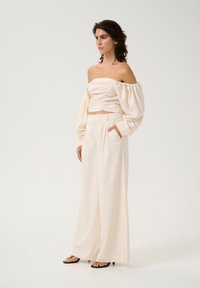 Cream off-the-shoulder top with ruched detailing, paired with high-waisted wide-leg trousers, both in a soft, textured fabric.