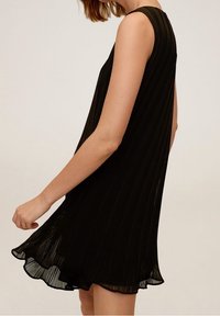 Robe noire sans manches avec un tissu plissé, une silhouette fluide et un ourlet légèrement arrondi. La texture semble légère et aérienne.