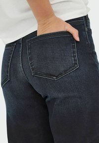 Donkere spijkerbroeken met een strakke pasvorm, met twee achterzakken en opvallende stiksels. Het materiaal heeft een gladde textuur met een lichte glans.