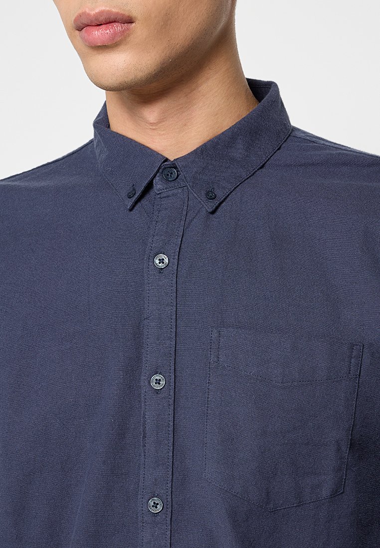 Marineblaues Hemd mit Knöpfen aus strukturiertem Stoff, ausgestattet mit einem klassischen Kragen, einer Brusttasche und dunklen Knöpfen mit Blumenmustern.