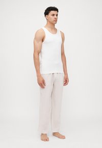 Top sin mangas de algodón blanco combinado con pantalones sueltos de lino beige claro, que presentan una textura suave y un diseño de pierna recta.